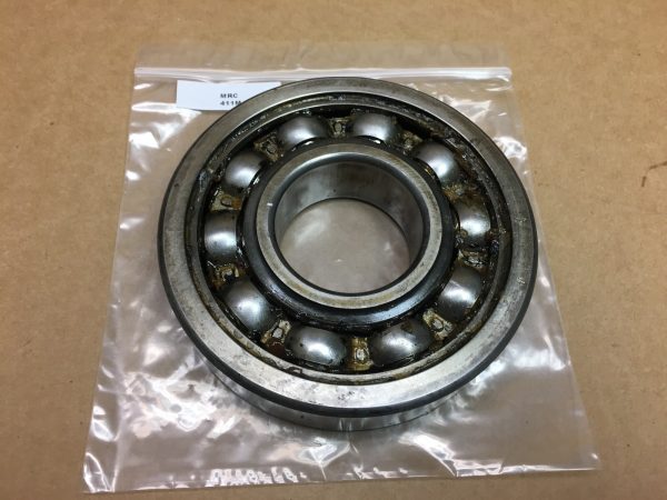 MRC 411M deep groove ball bearing, 55x140x33mm, open, in a plastic bag on a tan surface