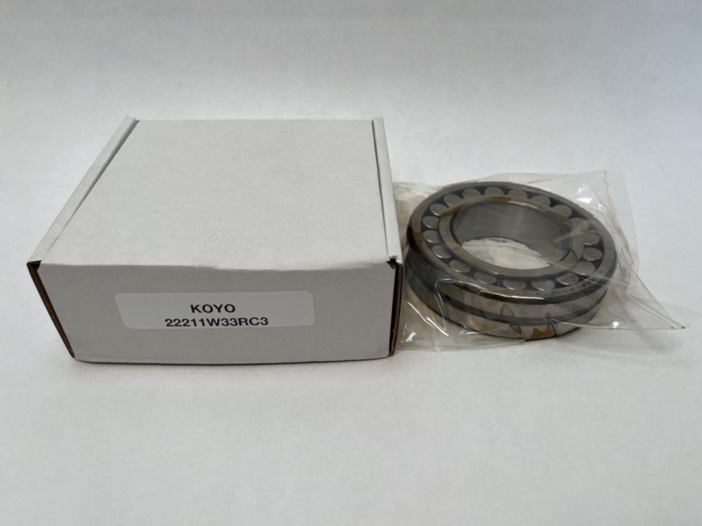 Koyo 22211RW33C3 spherical roller bearing in plastic packaging next to its labeled box
