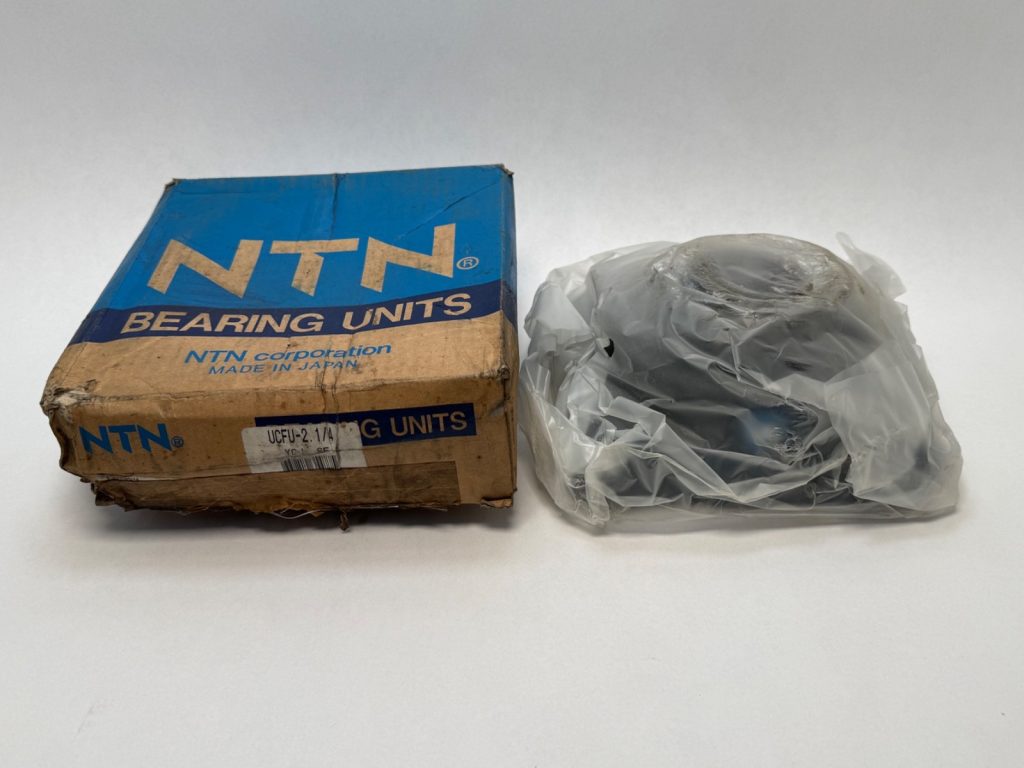 NTN UCFU-2-1/4 bearing unit in original box next to the flange bearing in plastic wrap